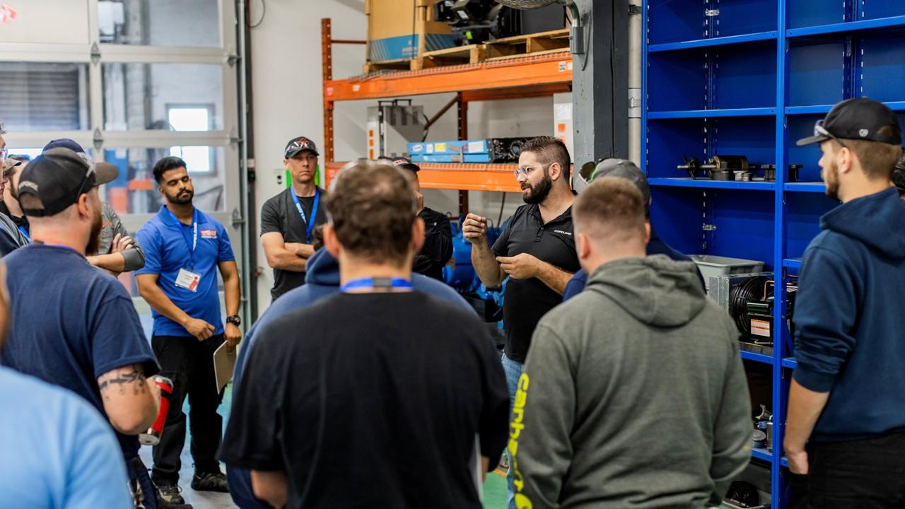 Instructor leading a group discussion for a compressor teardown near industrial equipment